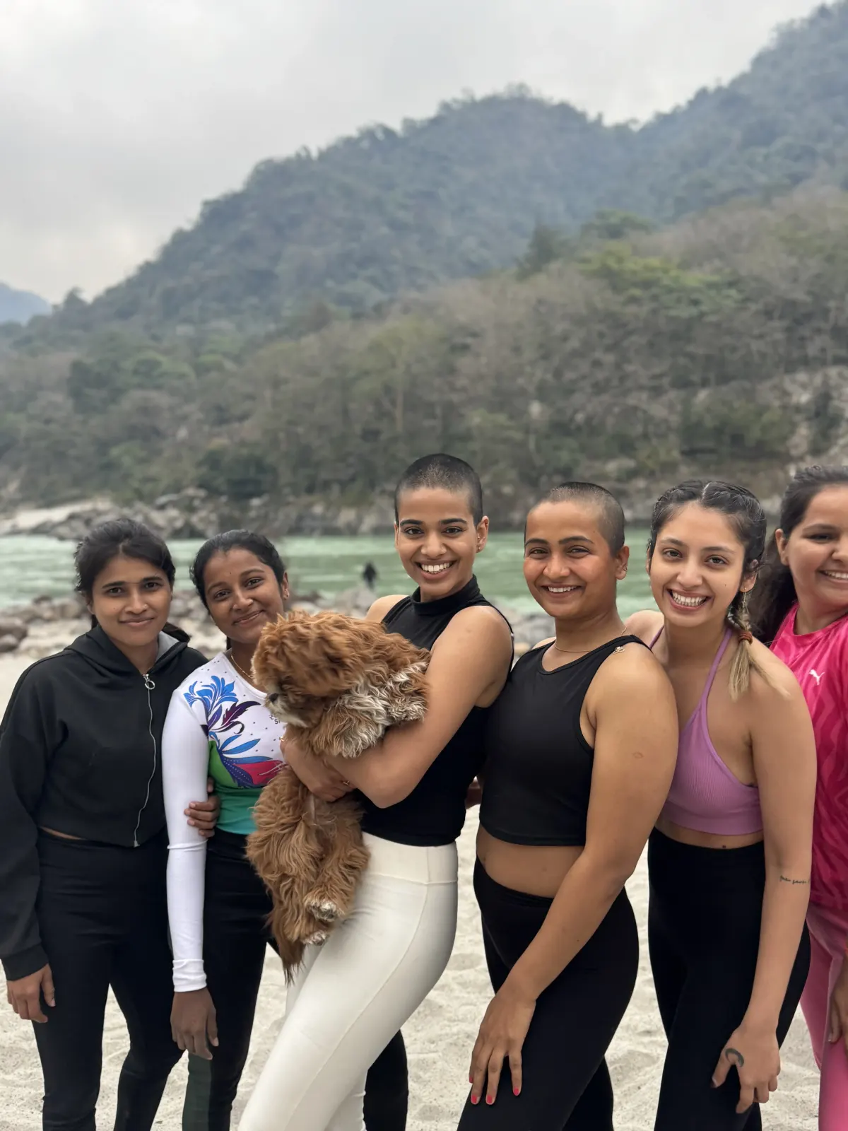 Smiling students posing with a fluffy dog by the Ganga river in Rishikesh