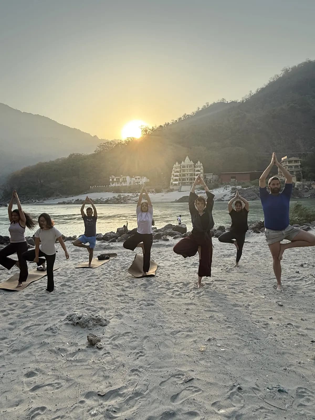 Students practising a standing asana at sunrise on the Ganga beach in Rishikesh