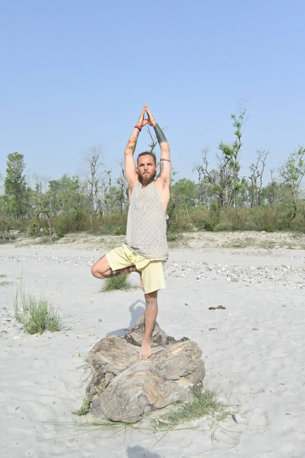 Student balancing in Tree pose on a river boulder on the Ganga beach in Rishikesh