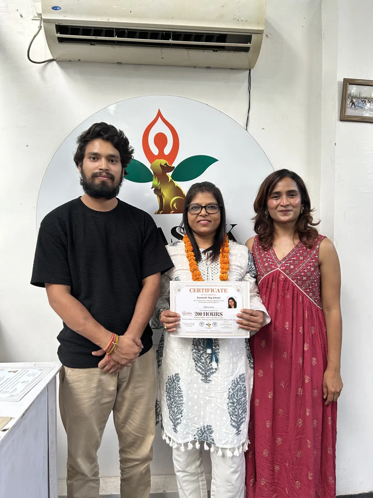 Graduate holding her 200 hours yoga teacher training certificate standing between two of her teachers at Swaastik Yog School