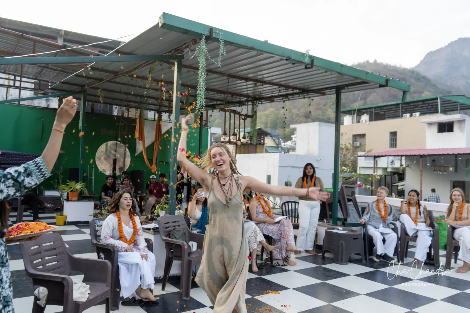 Graduate dancing with joy at the rooftop yoga teacher training graduation ceremony as garlanded classmates watch, Rishikesh
