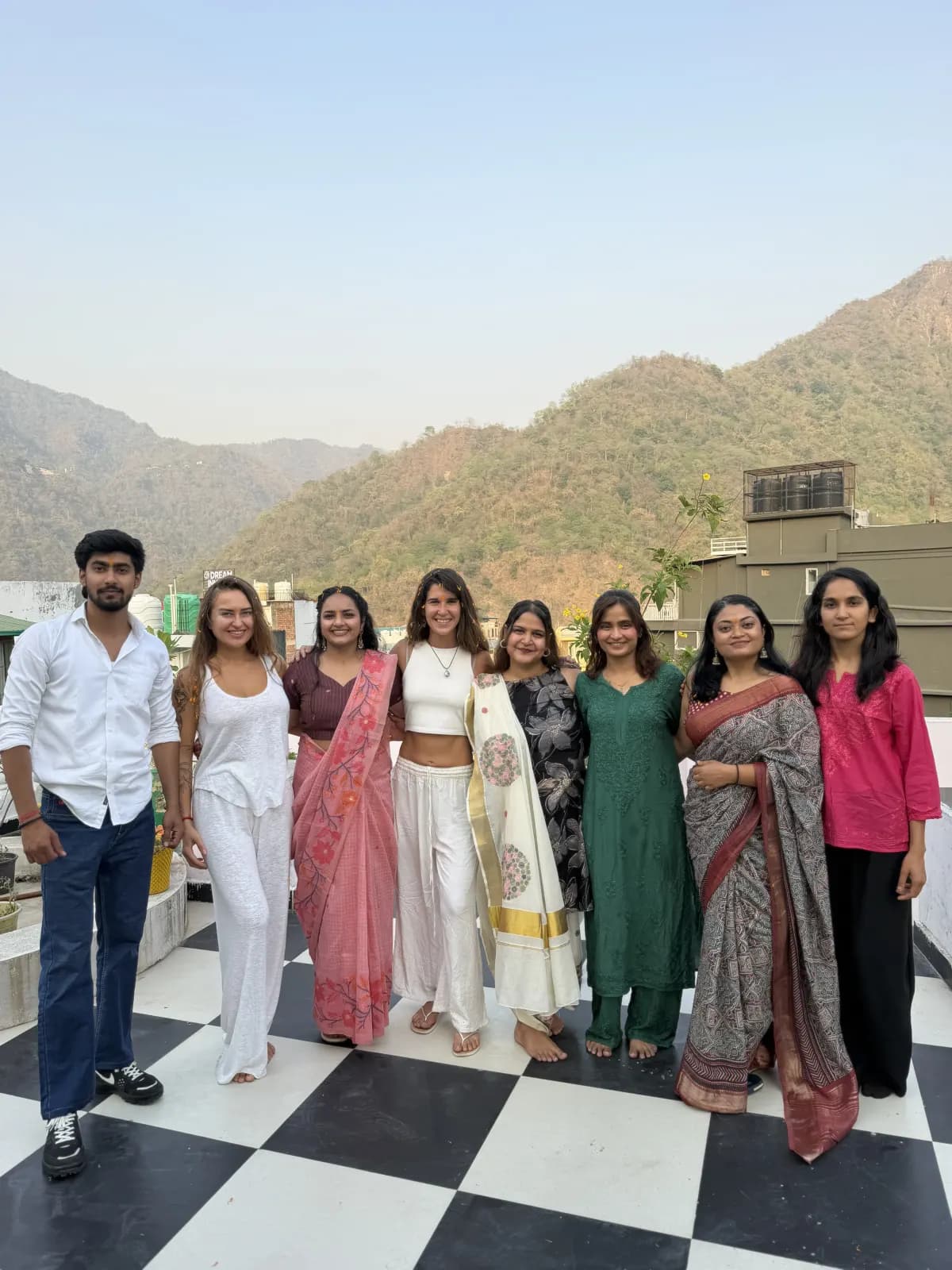 Yoga teacher training graduating class photo on the rooftop terrace with the Himalayan foothills behind, Rishikesh