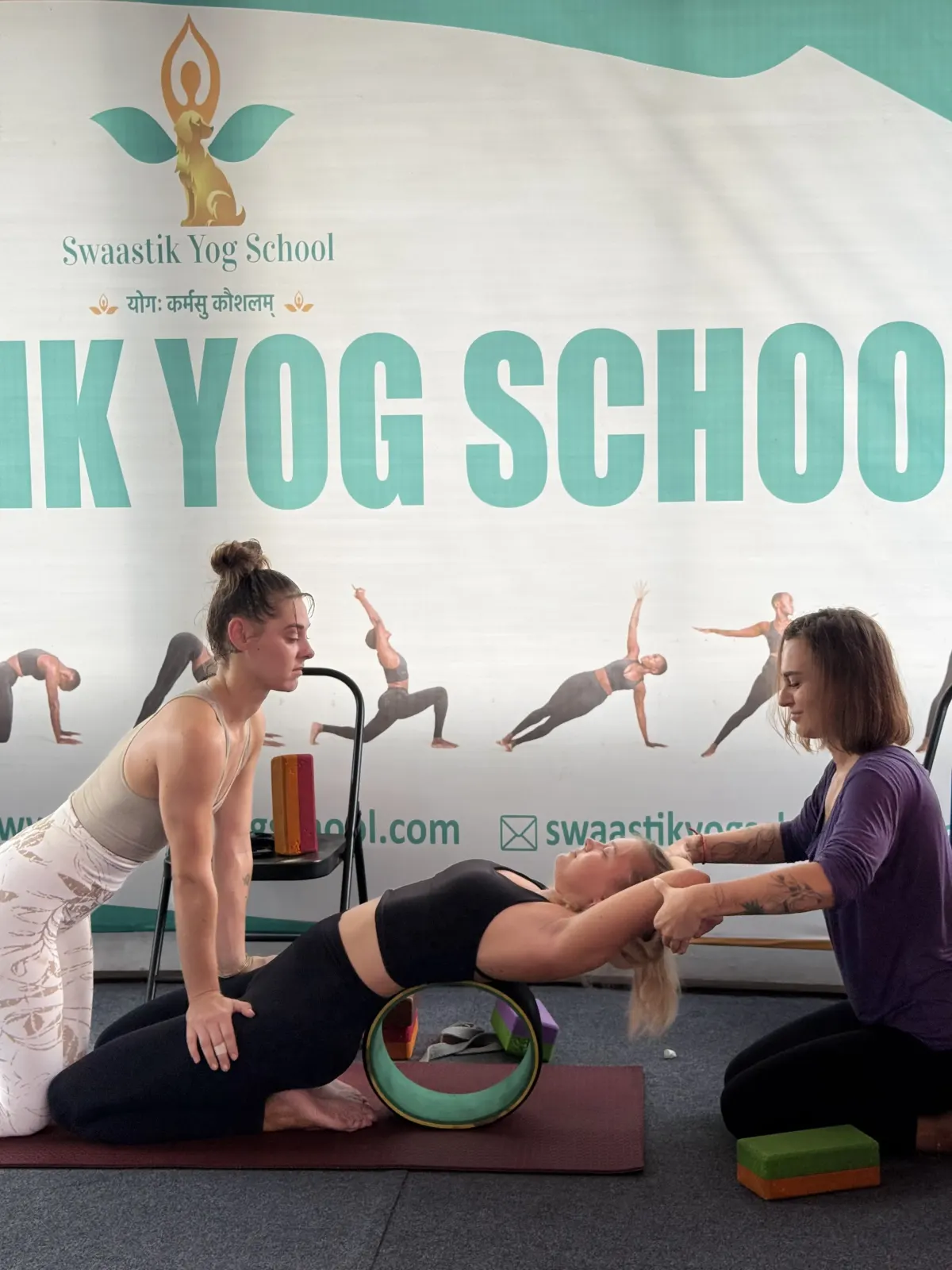 Yoga teacher supporting a student's backbend over a yoga wheel during teacher training in Rishikesh
