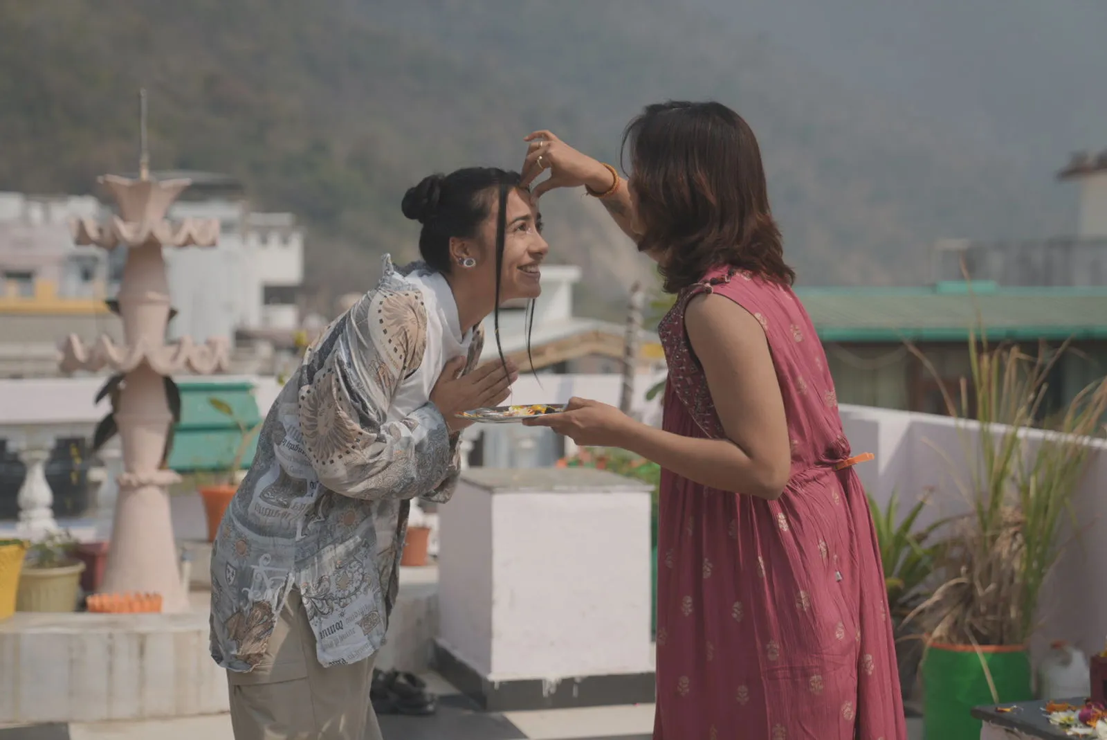 Traditional tilak blessing ceremony for a graduating yoga teacher on a rooftop with Himalayan foothills behind, Rishikesh