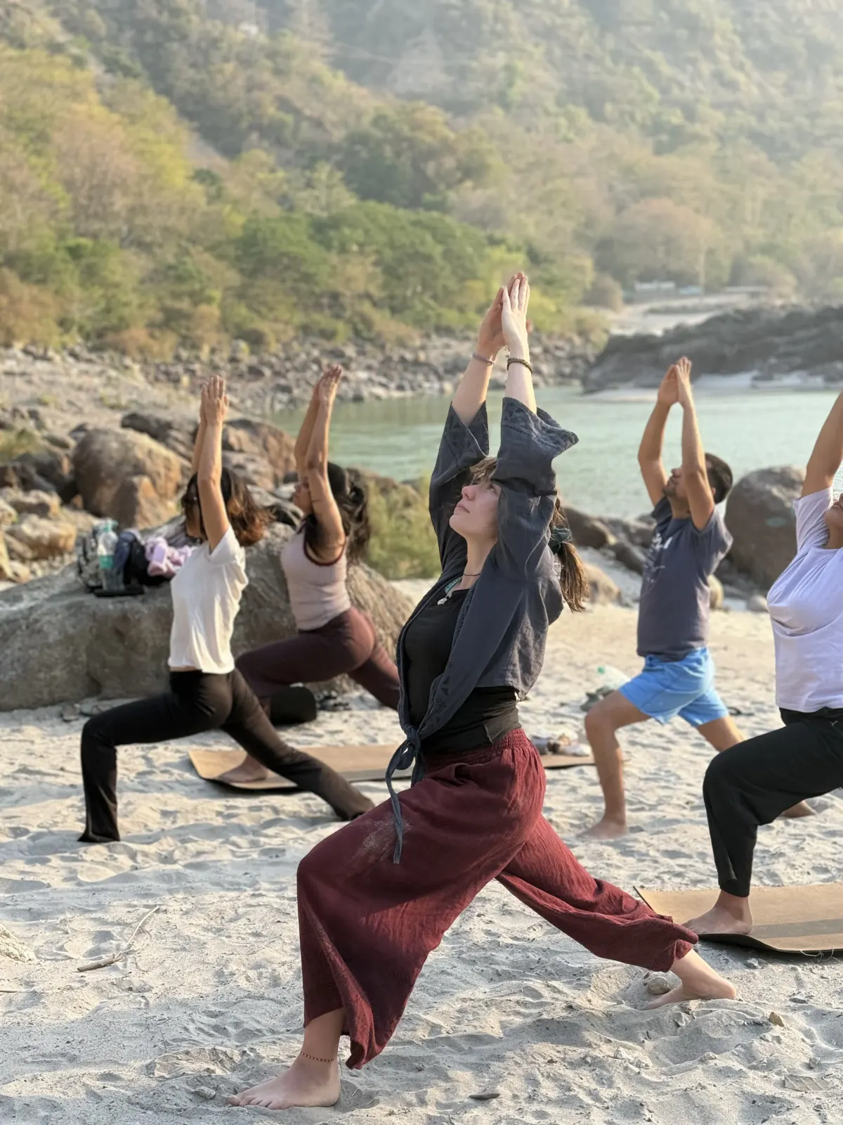 200 hour yoga teacher training students in a Crescent Lunge on the white-sand Ganga beach in Rishikesh