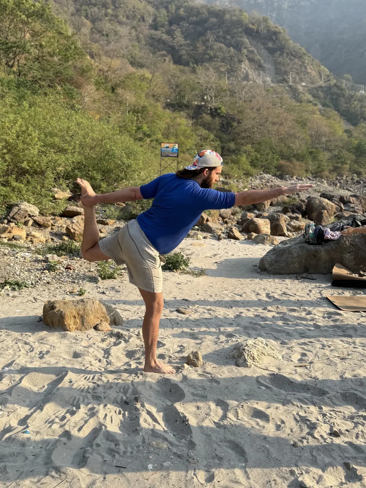 Trainee holding a standing balance on the Ganga beach during the asana module at Swaastik Yog School