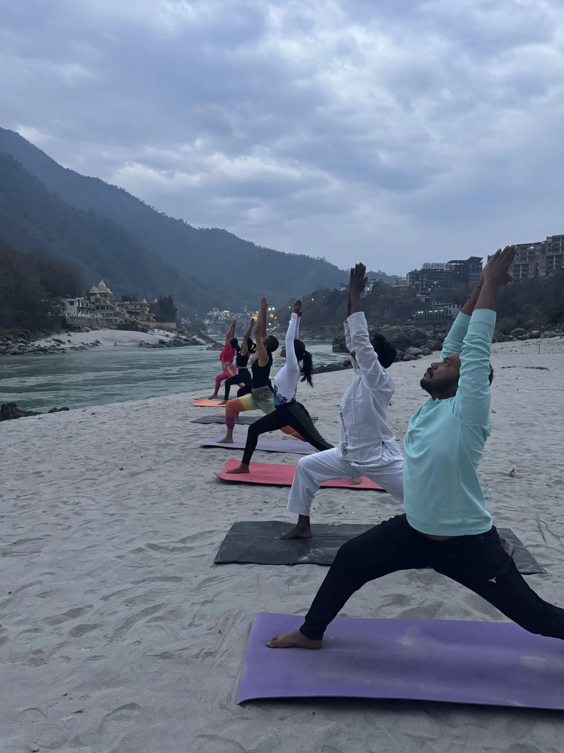 100 hour yoga teacher training students practising Warrior pose on the Ganga beach in Rishikesh