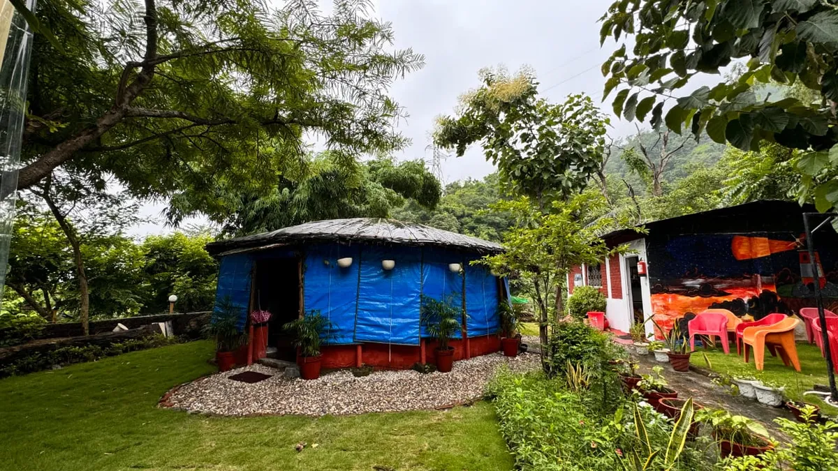Campus garden at Swaastik Yog School in Tapovan, Rishikesh, with a round hut, potted plants, trees and outdoor seating