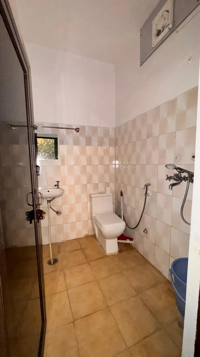 Attached private bathroom with a western toilet, wash basin and hand shower in a private room at the Tapovan yoga campus