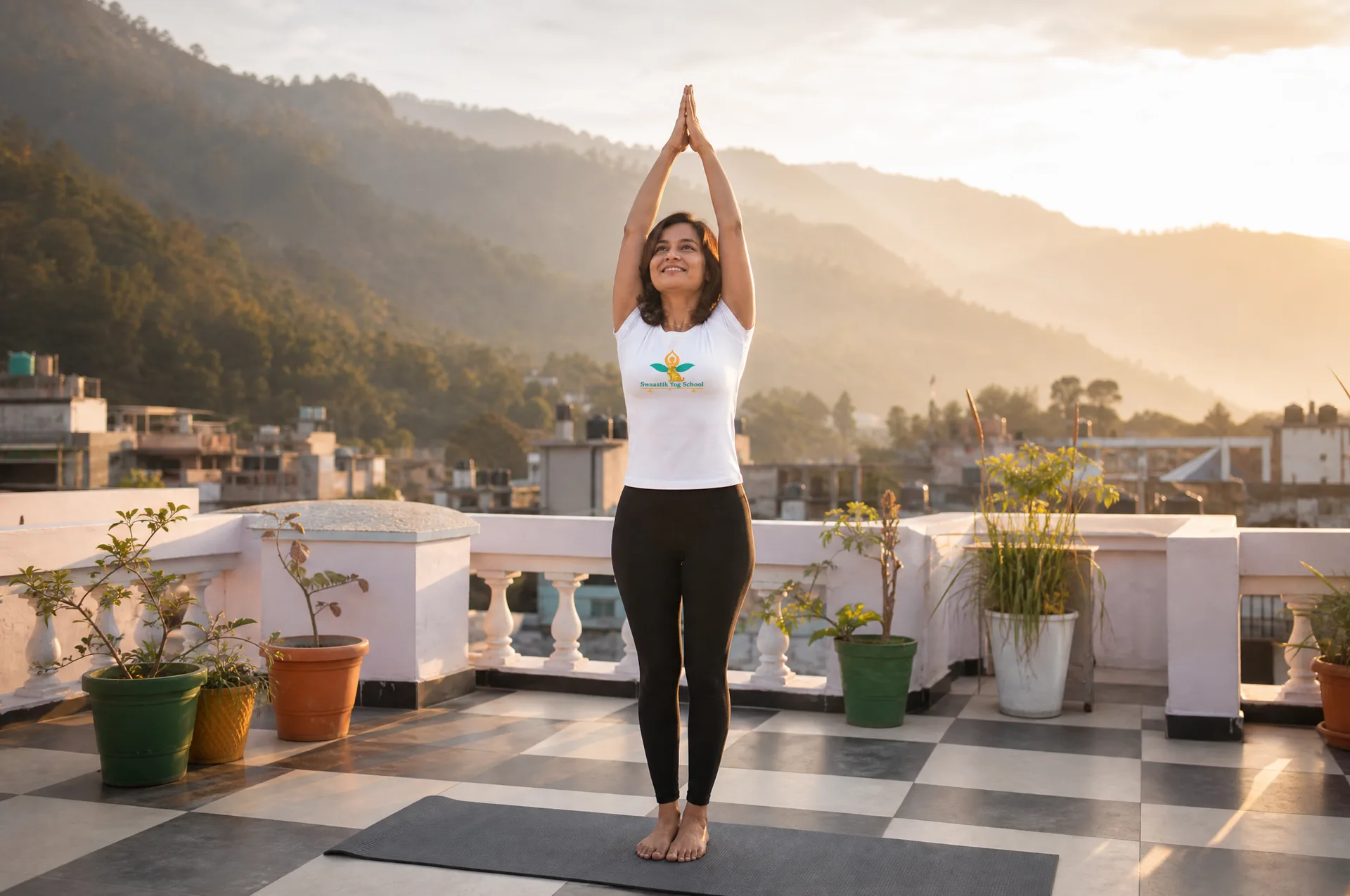 Mayuri reaching arms overhead in urdhva hastasana at sunrise on a rooftop overlooking misty Himalayan foothills in Rishikesh