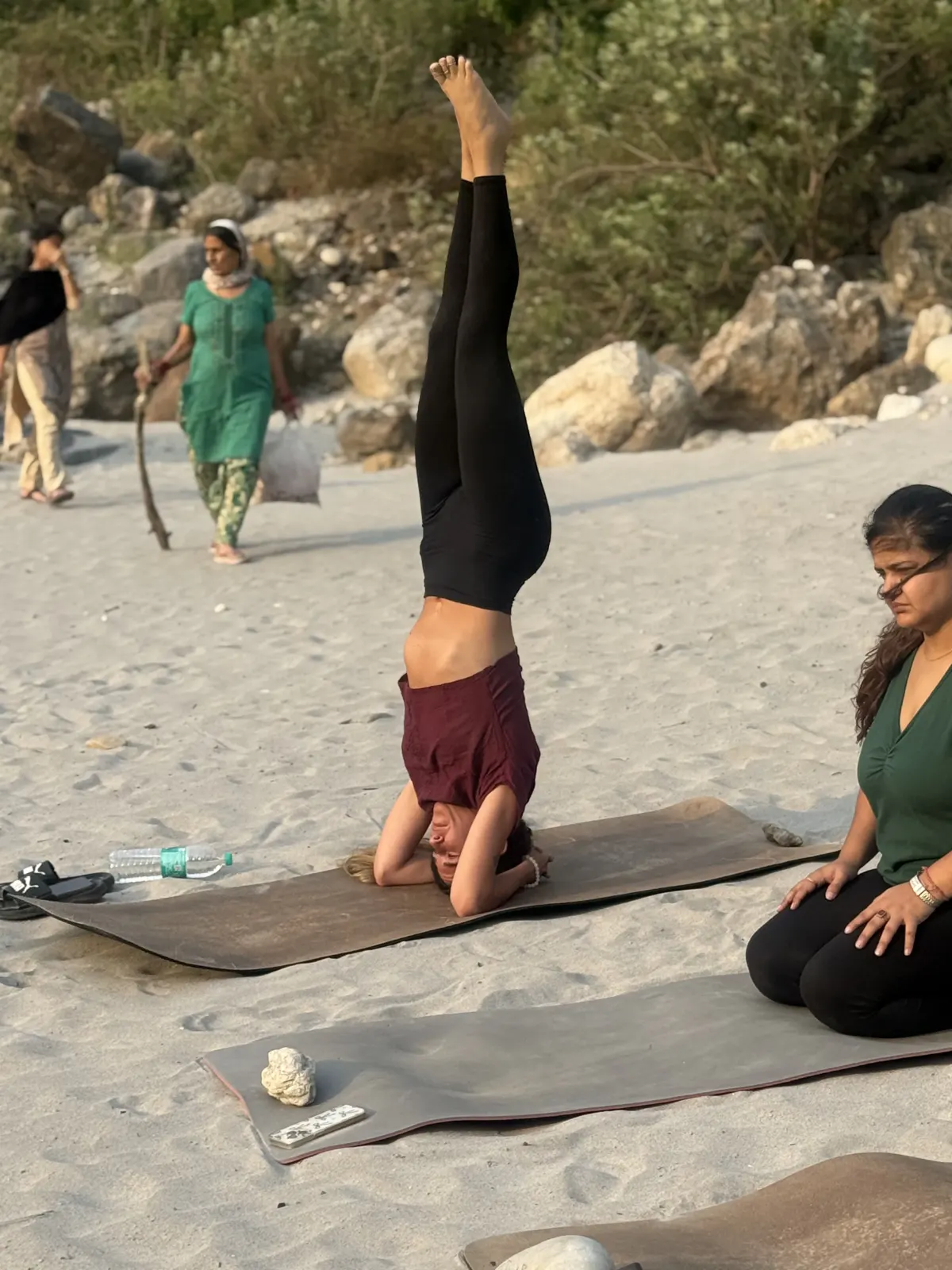 A yoga teacher training student holding a headstand on the sandy Ganga beach near Tapovan, Rishikesh, during an outdoor practice