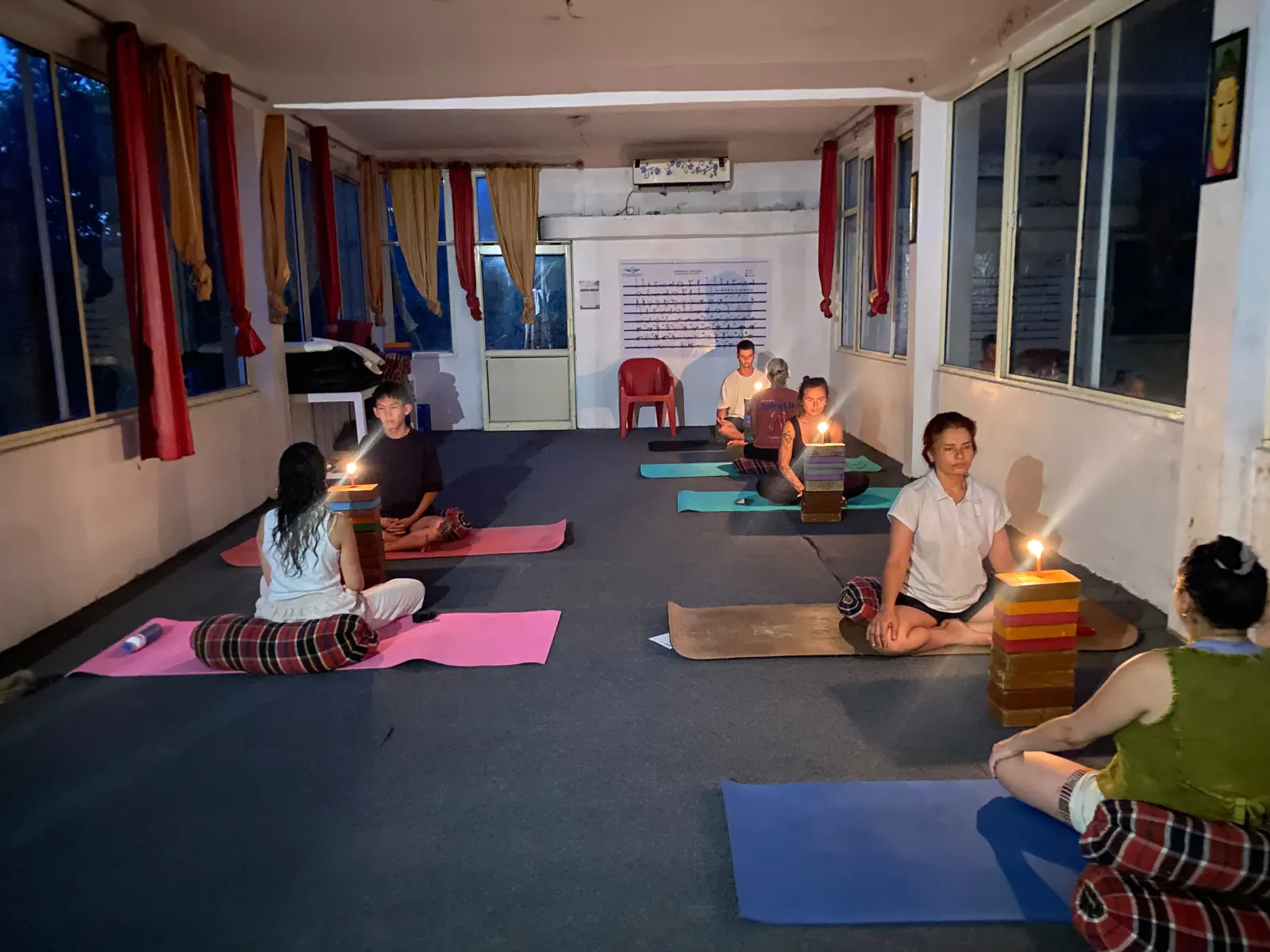 Students practising trataka candle-gazing meditation in the evening yoga hall at Swaastik Yog School